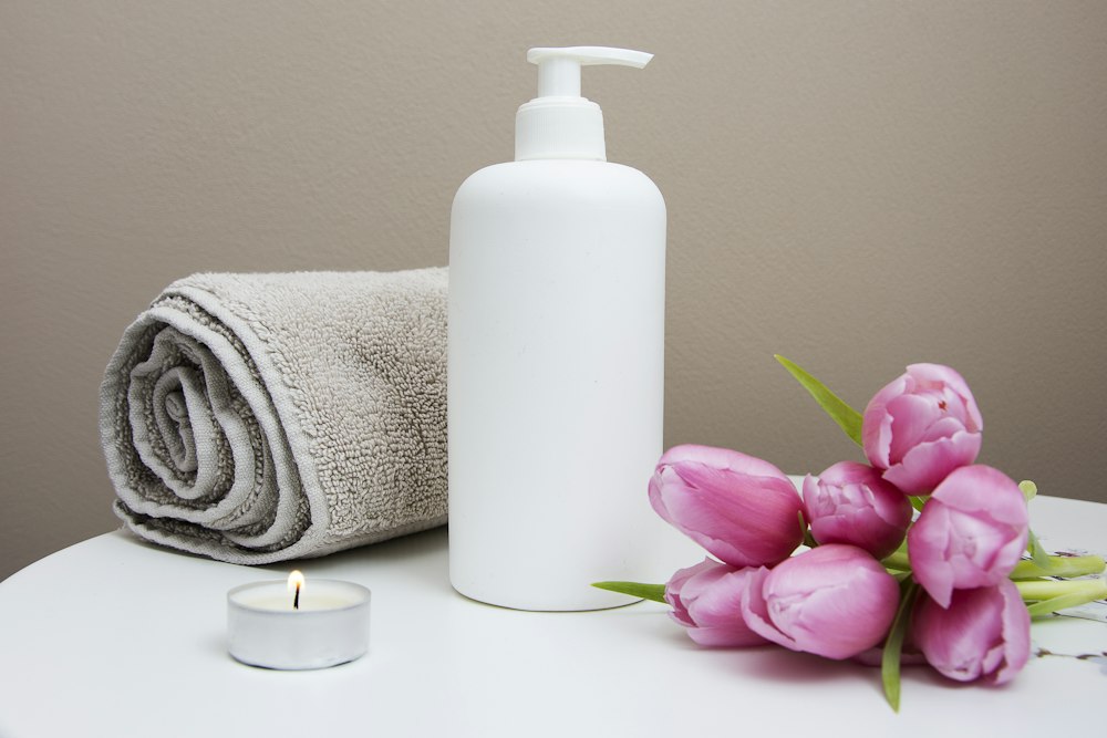 Massage oil bottle beside rolled towels and fresh tulips