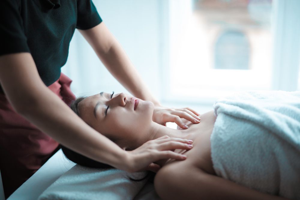 Woman lying face-up while a therapist massages her neck and head